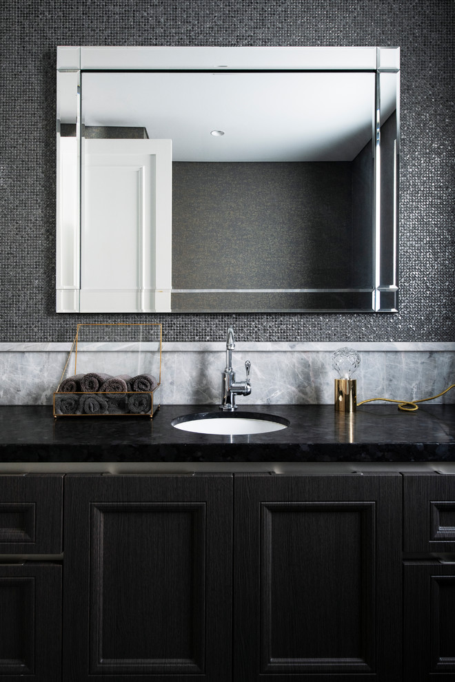 This is an example of a mid-sized traditional powder room in Sydney with raised-panel cabinets, dark wood cabinets, a one-piece toilet, gray tile, mosaic tile, marble floors, an undermount sink, granite benchtops, grey floor and black benchtops.