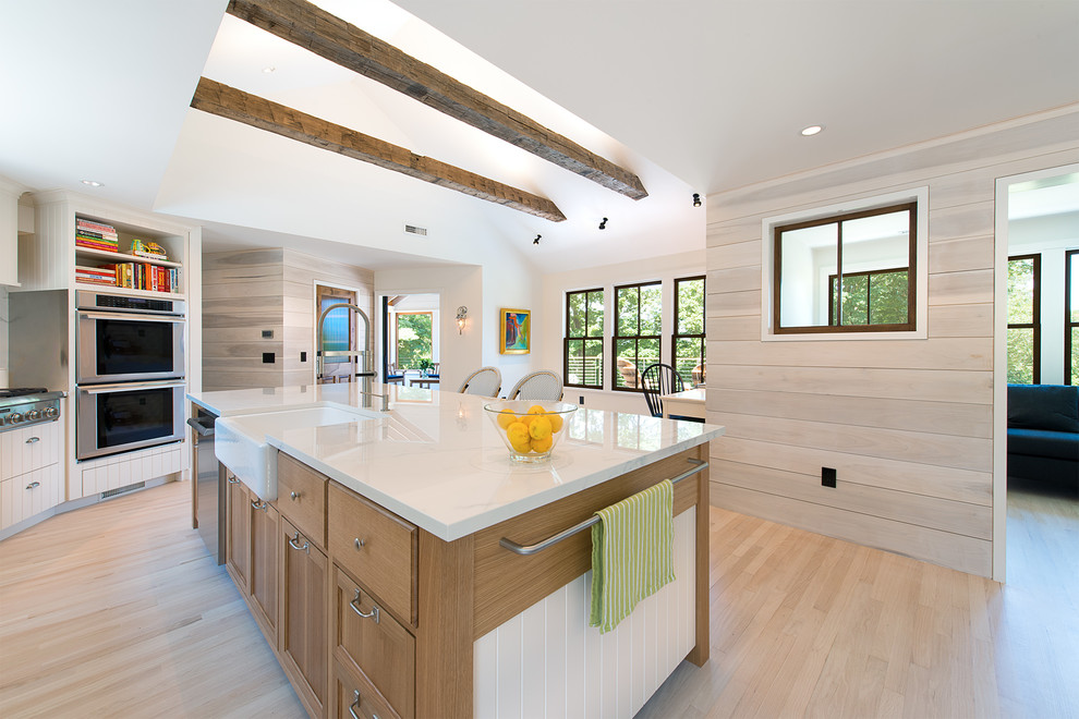 Photo of a large contemporary galley kitchen in New York with a farmhouse sink, marble benchtops, stainless steel appliances, light hardwood floors, with island, beige floor, recessed-panel cabinets and medium wood cabinets.