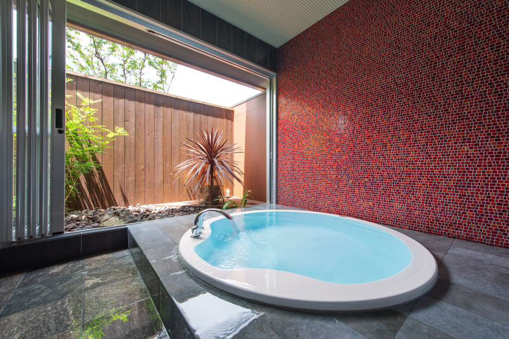 Photo of a bathroom with a hot tub, red tile, glass tile, red walls, porcelain floors and grey floor.