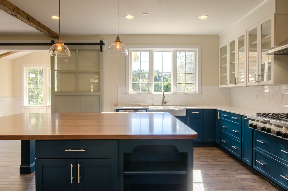 Country eat-in kitchen in Baltimore with a farmhouse sink, glass-front cabinets, blue cabinets, wood benchtops, white splashback, stainless steel appliances, dark hardwood floors, with island, brown floor and wood.