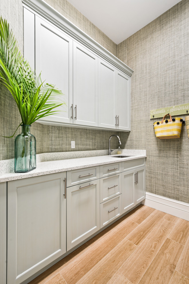 Inspiration for a large tropical u-shaped laundry room in Other with an undermount sink, beaded inset cabinets, white cabinets, quartzite benchtops, glass tile splashback, light hardwood floors, brown floor and beige benchtop.