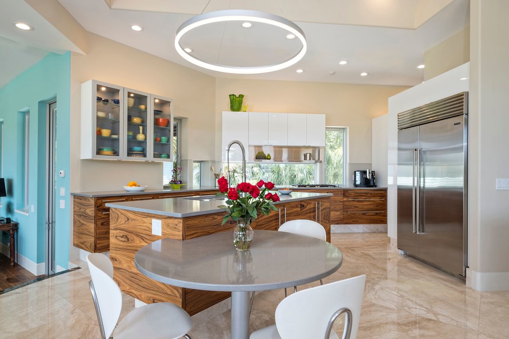 This is an example of a tropical kitchen in Miami with flat-panel cabinets, window splashback, stainless steel appliances, beige floor and dark wood cabinets.
