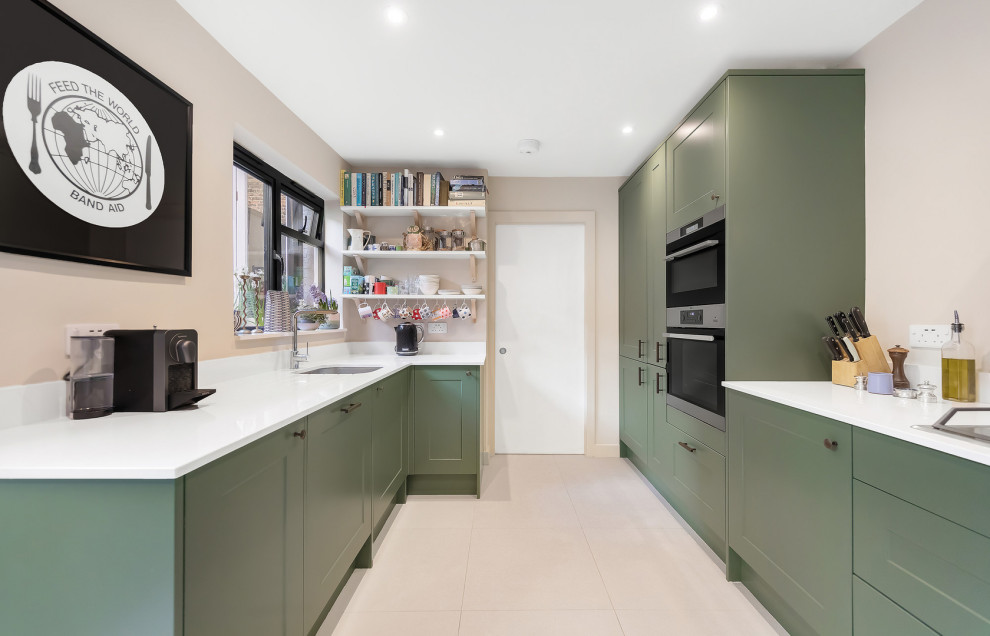 Inspiration for a mid-sized transitional u-shaped kitchen in London with an undermount sink, shaker cabinets, green cabinets, solid surface benchtops, panelled appliances, porcelain floors, no island, beige floor and white benchtop.