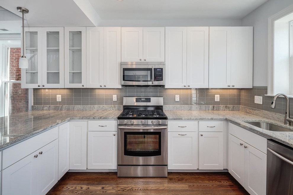 This is an example of a traditional u-shaped eat-in kitchen in Other with a single-bowl sink, white cabinets, grey splashback, glass tile splashback and stainless steel appliances.