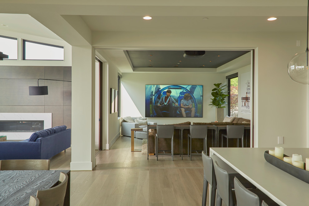 Photo of a mid-sized contemporary home theatre in Seattle with white walls, light hardwood floors and a projector screen.