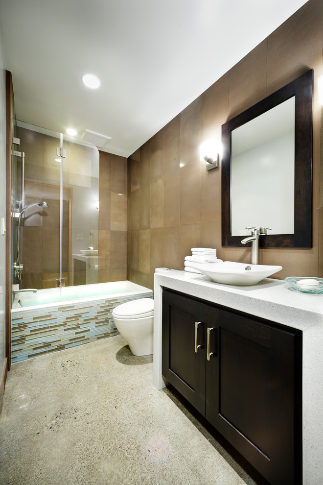 This is an example of a mid-sized contemporary bathroom in Sacramento with shaker cabinets, dark wood cabinets, an alcove tub, a shower/bathtub combo, a one-piece toilet, blue tile, brown tile, matchstick tile, brown walls, concrete floors, a vessel sink and quartzite benchtops.
