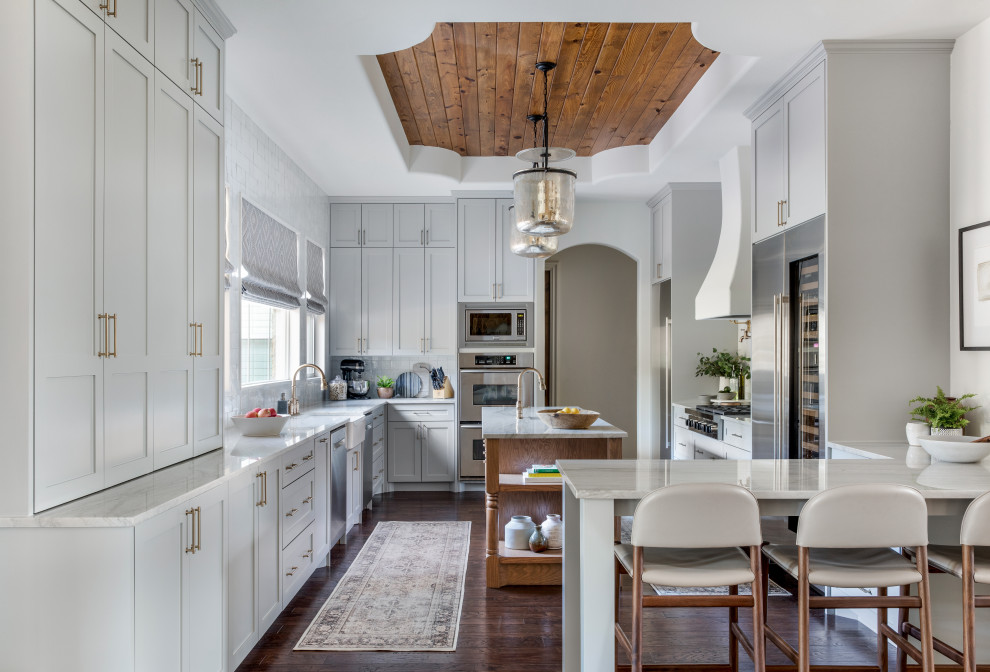 This is an example of a mid-sized transitional u-shaped eat-in kitchen in Austin with an undermount sink, shaker cabinets, white cabinets, granite benchtops, stainless steel appliances, medium hardwood floors, with island and white benchtop.
