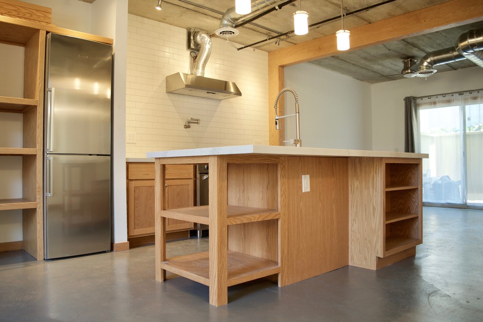 This is an example of a small industrial single-wall eat-in kitchen in Phoenix with a farmhouse sink, shaker cabinets, light wood cabinets, quartzite benchtops, white splashback, subway tile splashback, stainless steel appliances, concrete floors, with island and grey floor.