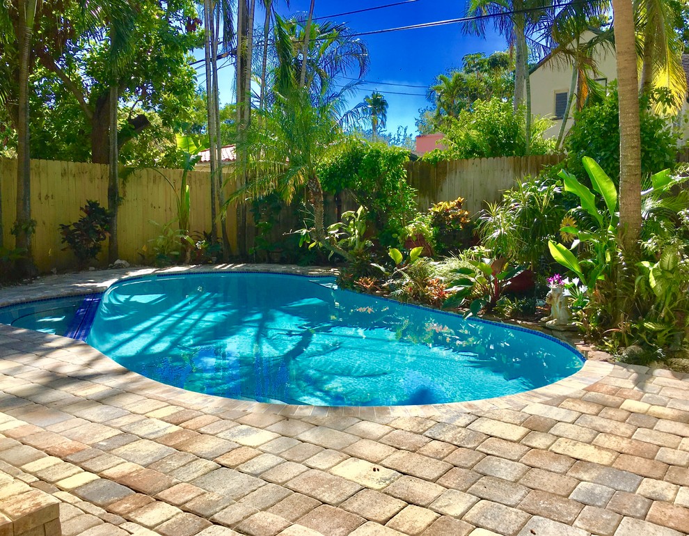 Design ideas for a large backyard kidney-shaped lap pool in Miami with brick pavers.