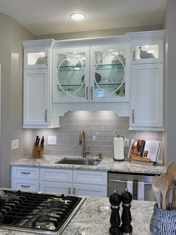 Mid-sized transitional light wood floor and brown floor eat-in kitchen photo in DC Metro with an undermount sink, glass-front cabinets, white cabinets, granite countertops, gray backsplash, subway tile backsplash, stainless steel appliances, an island and white countertops