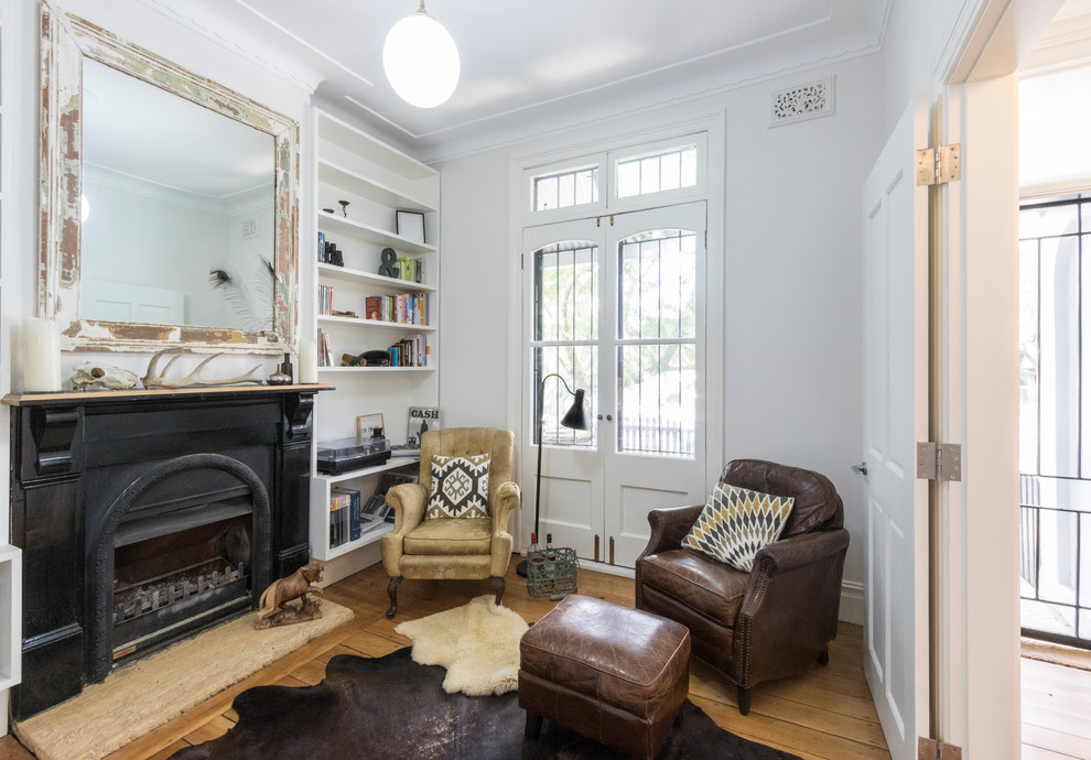 Design ideas for a small contemporary enclosed living room in Other with a library, white walls, light hardwood floors, a standard fireplace, a metal fireplace surround and a freestanding tv.