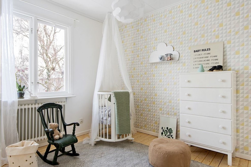 Design ideas for a mid-sized scandinavian gender-neutral nursery in Stockholm with multi-coloured walls and light hardwood floors.