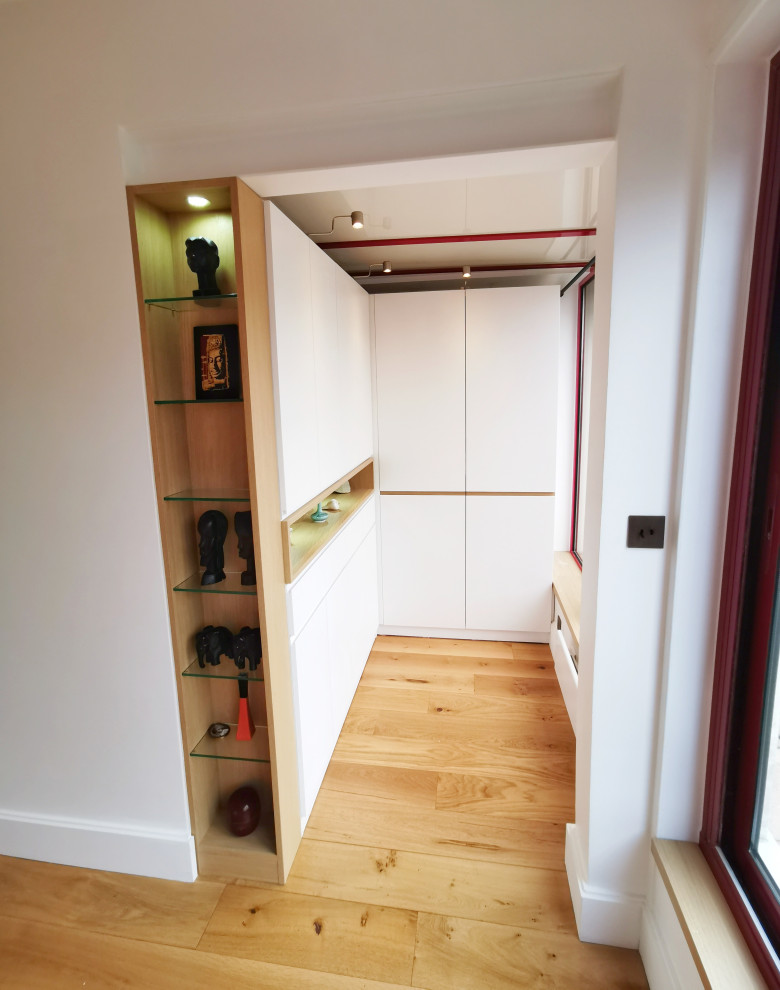 Inspiration for a mid-sized modern women's walk-in wardrobe in Paris with flat-panel cabinets, light wood cabinets, light hardwood floors and brown floor.
