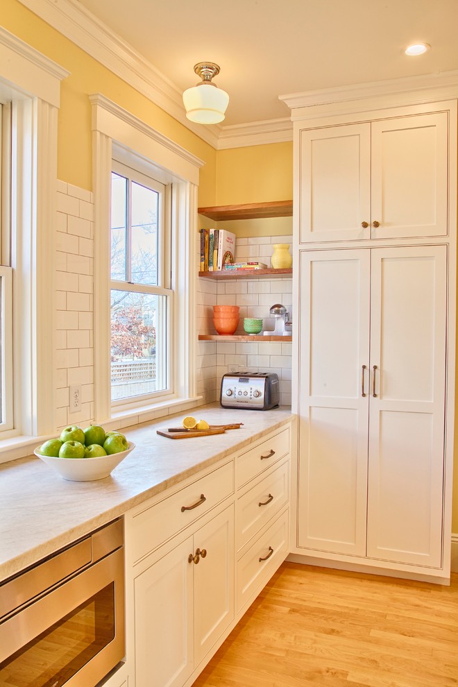 Design ideas for a mid-sized transitional l-shaped separate kitchen in Boston with an undermount sink, shaker cabinets, white cabinets, quartzite benchtops, white splashback, subway tile splashback, stainless steel appliances, medium hardwood floors, with island and brown floor.