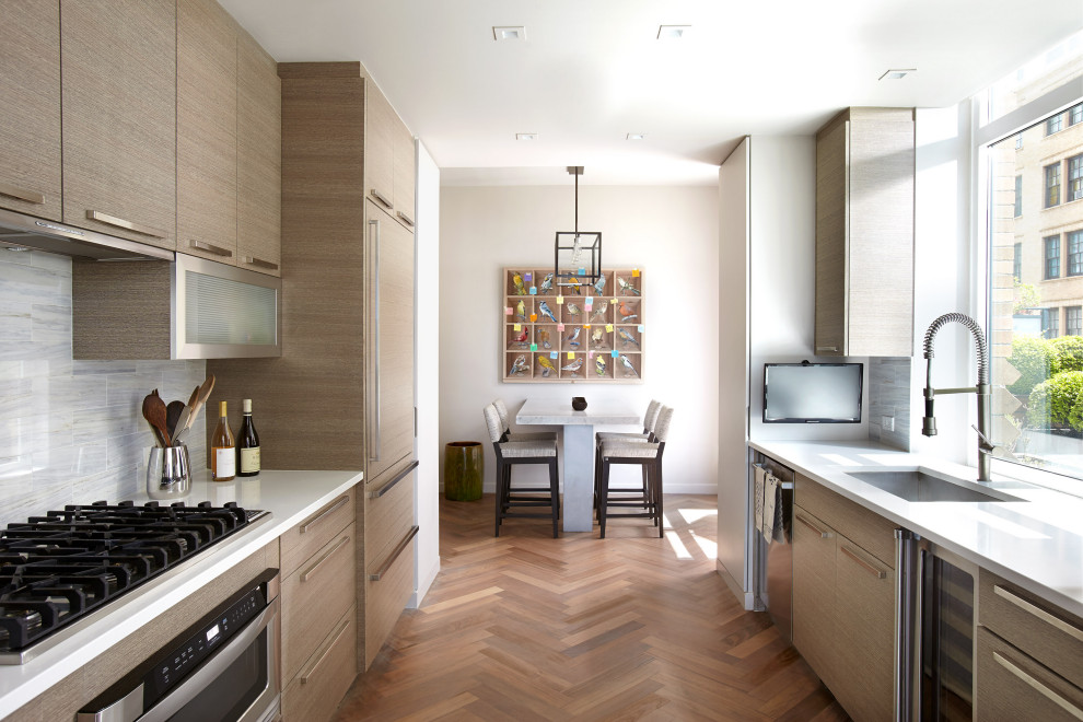 Photo of a large contemporary galley eat-in kitchen in New York with an undermount sink, flat-panel cabinets, light wood cabinets, solid surface benchtops, grey splashback, stainless steel appliances, medium hardwood floors, white benchtop, glass tile splashback, no island and brown floor.