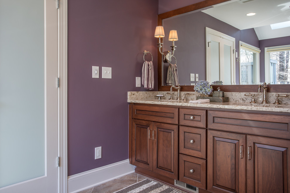 This is an example of a mid-sized traditional bathroom in Raleigh with an undermount sink, raised-panel cabinets, medium wood cabinets, quartzite benchtops, a drop-in tub, beige tile, porcelain tile, purple walls and porcelain floors.