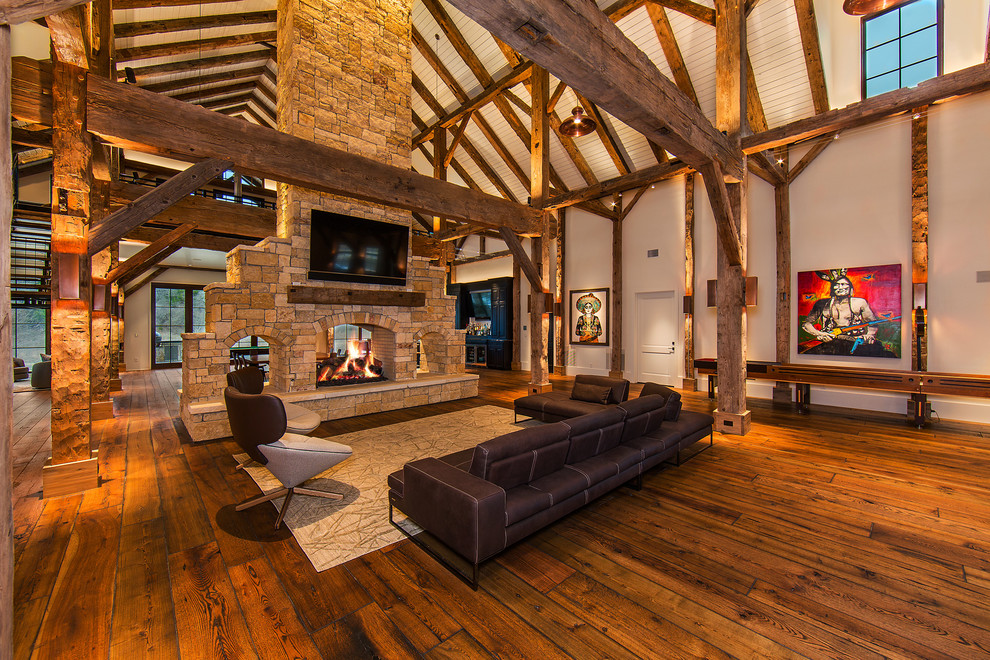 Photo of a large country open concept living room in Austin with white walls, medium hardwood floors, a two-sided fireplace, a stone fireplace surround, brown floor and a wall-mounted tv.