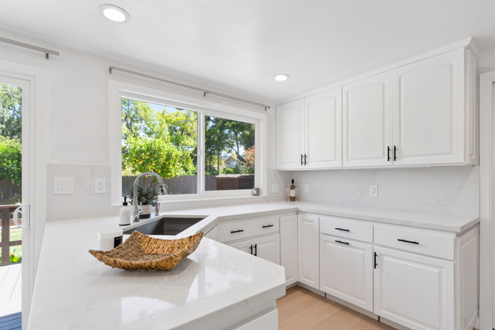 Mid-sized modern u-shaped eat-in kitchen in San Francisco with a farmhouse sink, shaker cabinets, white cabinets, marble benchtops, grey splashback, marble splashback, stainless steel appliances, vinyl floors, a peninsula, beige floor and grey benchtop.