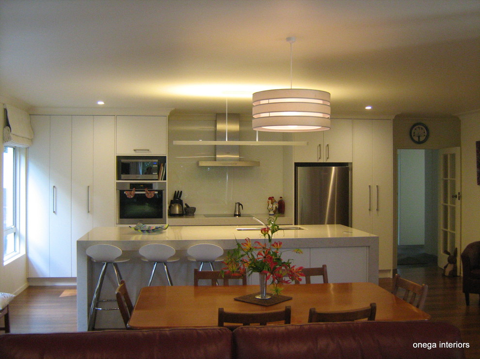 Inspiration for a modern kitchen in Napier-Hastings with white cabinets, quartz benchtops, white splashback, glass sheet splashback, with island, a double-bowl sink and medium hardwood floors.