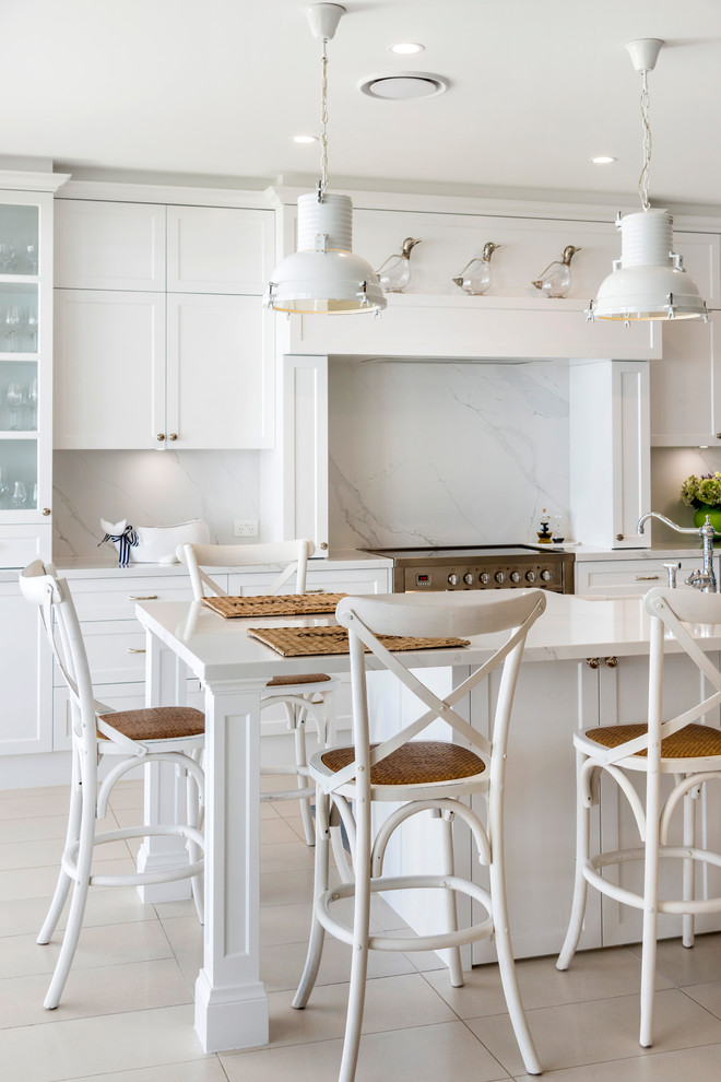 Design ideas for a large beach style galley eat-in kitchen in Gold Coast - Tweed with a farmhouse sink, shaker cabinets, white cabinets, marble benchtops, white splashback, marble splashback, stainless steel appliances, ceramic floors, with island, beige floor and white benchtop.
