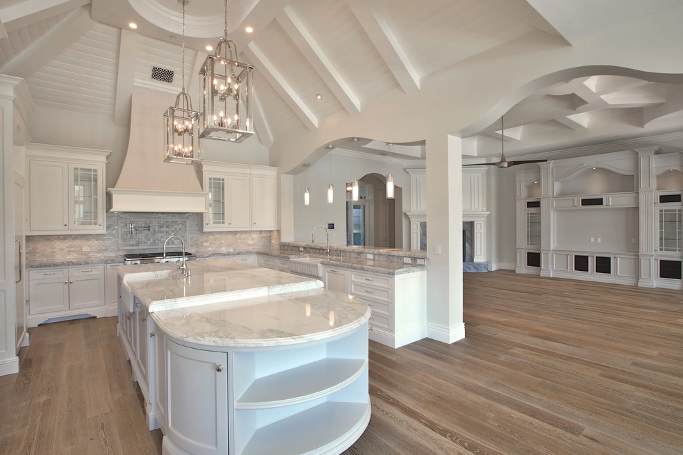 Open concept kitchen - huge transitional u-shaped light wood floor open concept kitchen idea in Phoenix with a farmhouse sink, shaker cabinets, white cabinets, marble countertops, gray backsplash, glass tile backsplash, stainless steel appliances and an island