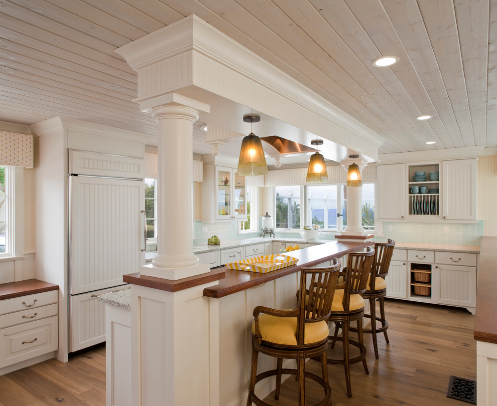 This is an example of a beach style l-shaped kitchen in San Diego with recessed-panel cabinets, white cabinets, blue splashback, panelled appliances and medium hardwood floors.