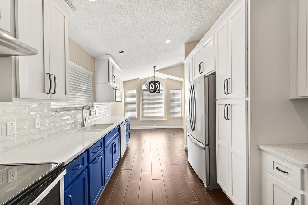 Large transitional l-shaped vinyl floor and brown floor open concept kitchen photo in Jacksonville with an undermount sink, shaker cabinets, blue cabinets, quartzite countertops, white backsplash, ceramic backsplash, stainless steel appliances and a peninsula