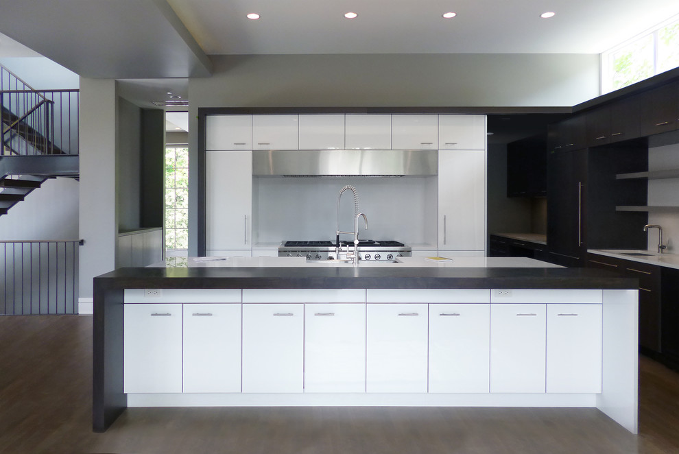 This is an example of a mid-sized modern l-shaped open plan kitchen in Chicago with a farmhouse sink, flat-panel cabinets, white cabinets, quartz benchtops, white splashback, panelled appliances, medium hardwood floors, with island, stone slab splashback, brown floor and white benchtop.