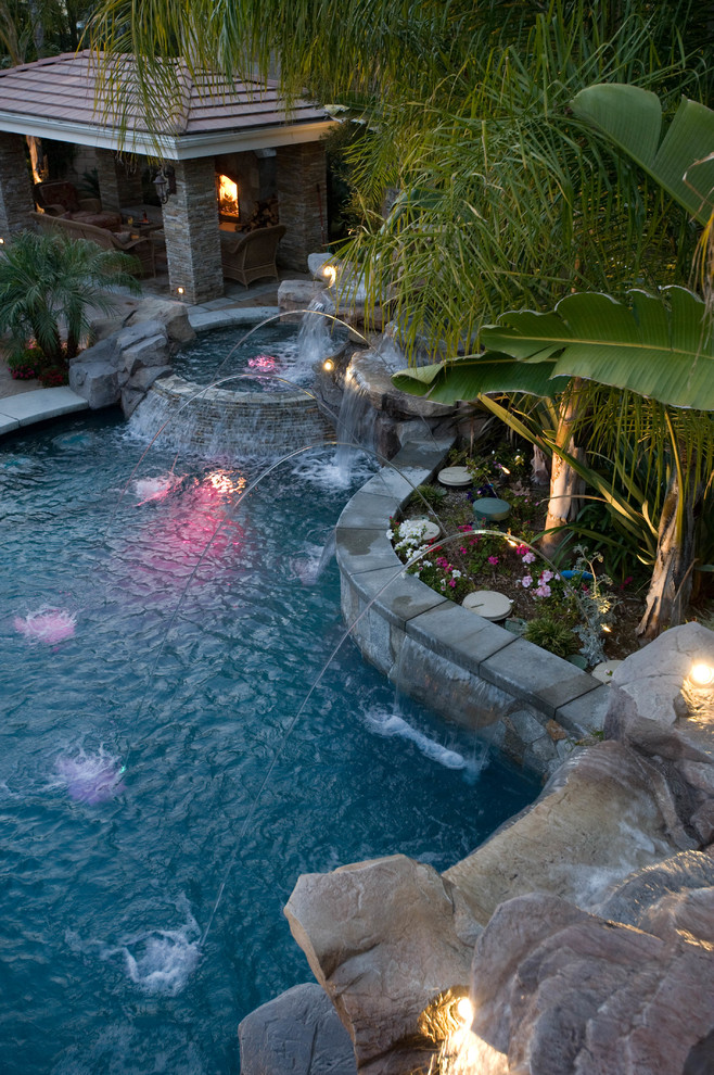 This is an example of a large tropical backyard custom-shaped pool in Los Angeles with a water feature and stamped concrete.