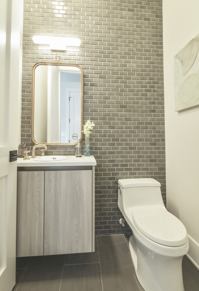 Small contemporary powder room in Chicago with furniture-like cabinets, medium wood cabinets, a one-piece toilet, gray tile, ceramic tile, white walls, ceramic floors, a drop-in sink, engineered quartz benchtops, grey floor and white benchtops.