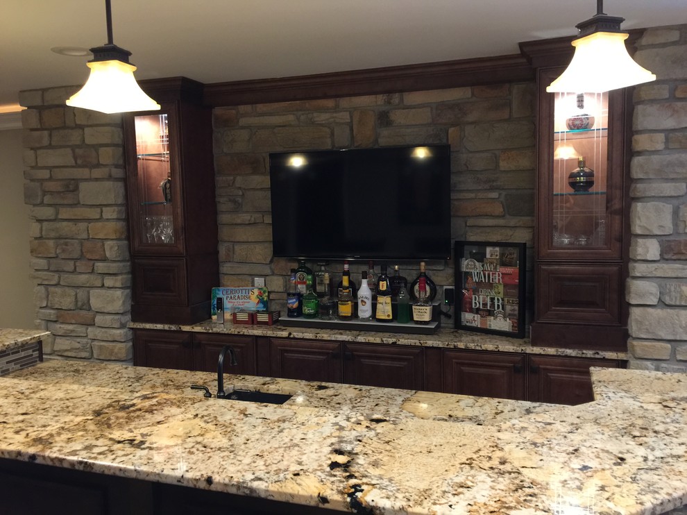 This is an example of a large arts and crafts single-wall seated home bar in St Louis with an undermount sink, raised-panel cabinets, granite benchtops, beige splashback, stone tile splashback, ceramic floors and dark wood cabinets.