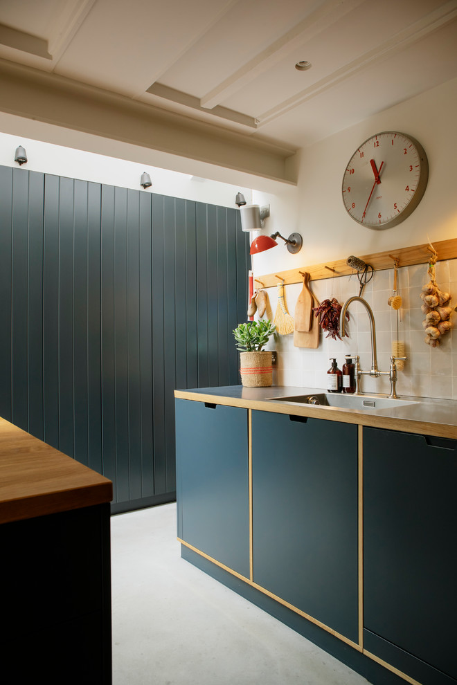 Inspiration for a mid-sized transitional eat-in kitchen in London with an integrated sink, flat-panel cabinets, blue cabinets, stainless steel benchtops, beige splashback, porcelain splashback, panelled appliances, concrete floors, with island and grey floor.