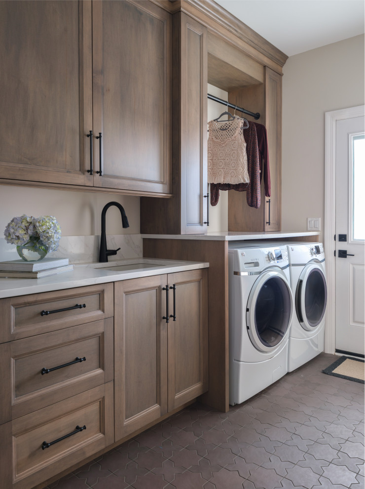 Transitional single-wall gray floor dedicated laundry room photo in St Louis with an undermount sink, recessed-panel cabinets, medium tone wood cabinets, beige walls, a side-by-side washer/dryer and white countertops