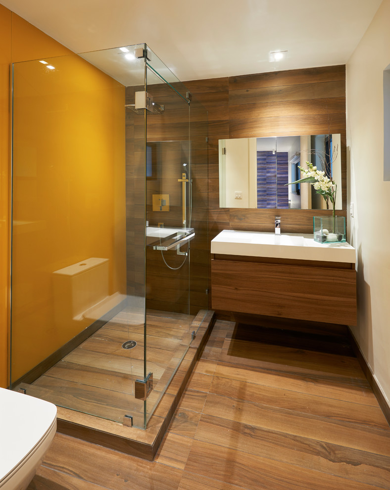 This is an example of a mid-sized contemporary bathroom in Miami with flat-panel cabinets, medium wood cabinets, a corner shower, a one-piece toilet, ceramic tile, orange walls, ceramic floors, a wall-mount sink and engineered quartz benchtops.