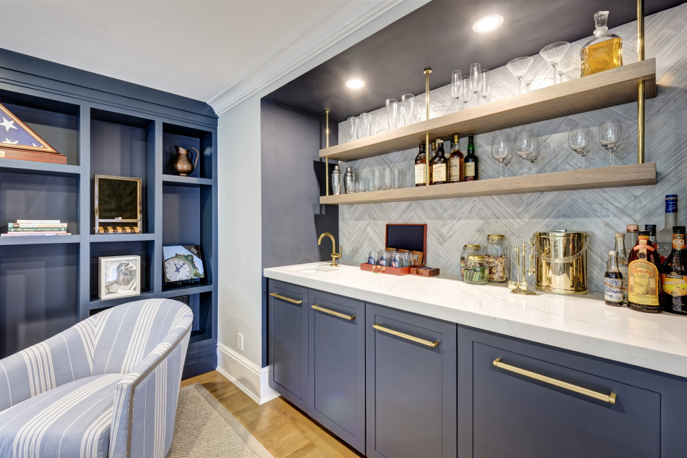 Photo of a medium sized beach style single-wall wet bar in New York with a submerged sink, shaker cabinets, blue cabinets, engineered stone countertops, grey splashback, porcelain splashback, light hardwood flooring, brown floors and white worktops.