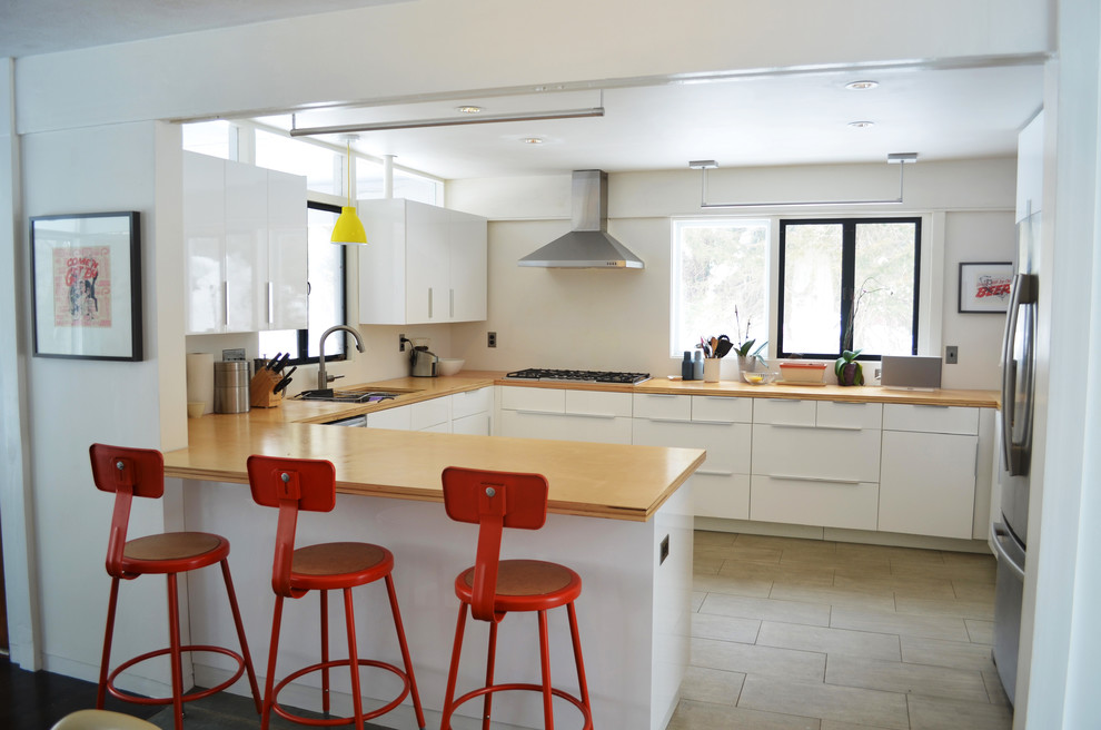 Mid-sized midcentury u-shaped eat-in kitchen in Boston with an undermount sink, flat-panel cabinets, white cabinets, wood benchtops, white splashback, stainless steel appliances, porcelain floors and a peninsula.