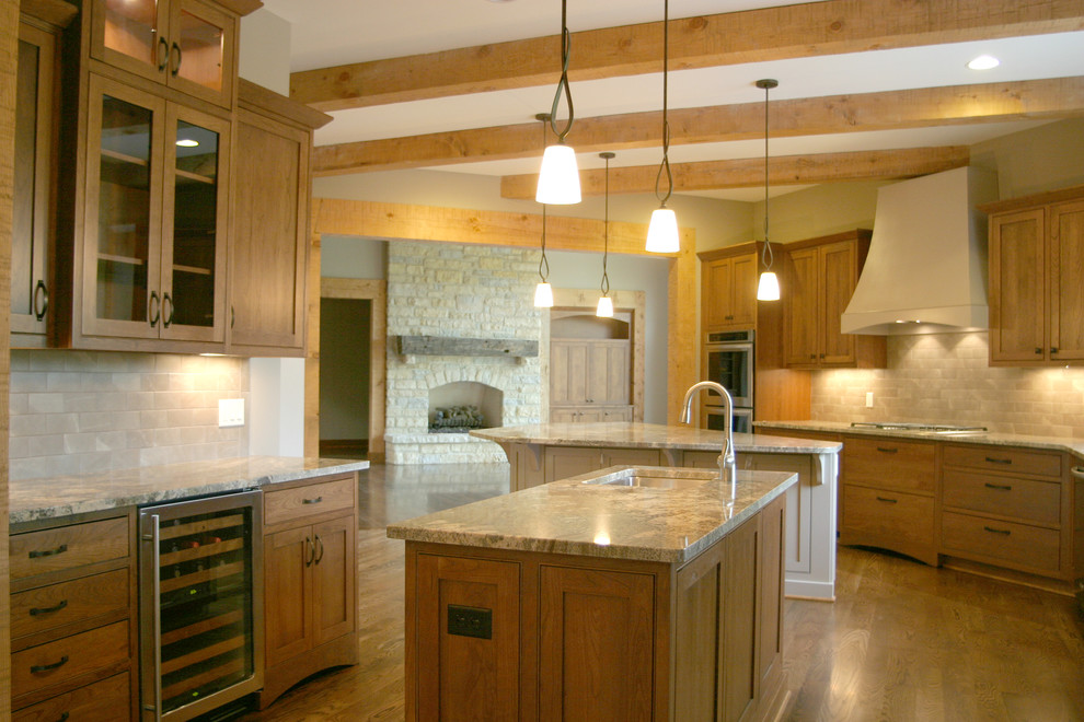 This is an example of an expansive arts and crafts u-shaped kitchen pantry in Cincinnati with medium wood cabinets, granite benchtops, beige splashback, stainless steel appliances, medium hardwood floors, multiple islands, an undermount sink, shaker cabinets and ceramic splashback.
