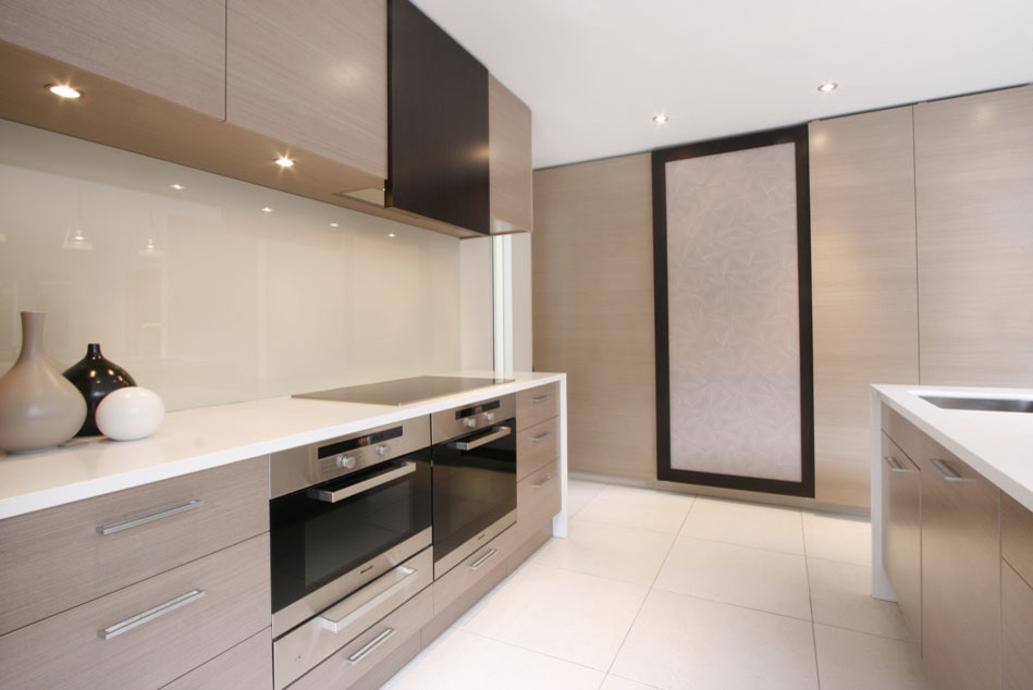 Inspiration for a contemporary l-shaped open plan kitchen in Auckland with an undermount sink, flat-panel cabinets, beige cabinets, quartz benchtops, beige splashback, glass sheet splashback, stainless steel appliances, porcelain floors and with island.
