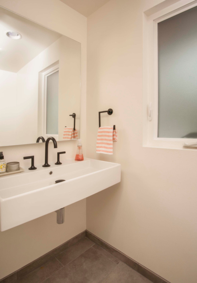 Photo of a small midcentury powder room in Seattle with open cabinets, a one-piece toilet, white tile, white walls, porcelain floors, a wall-mount sink and grey floor.