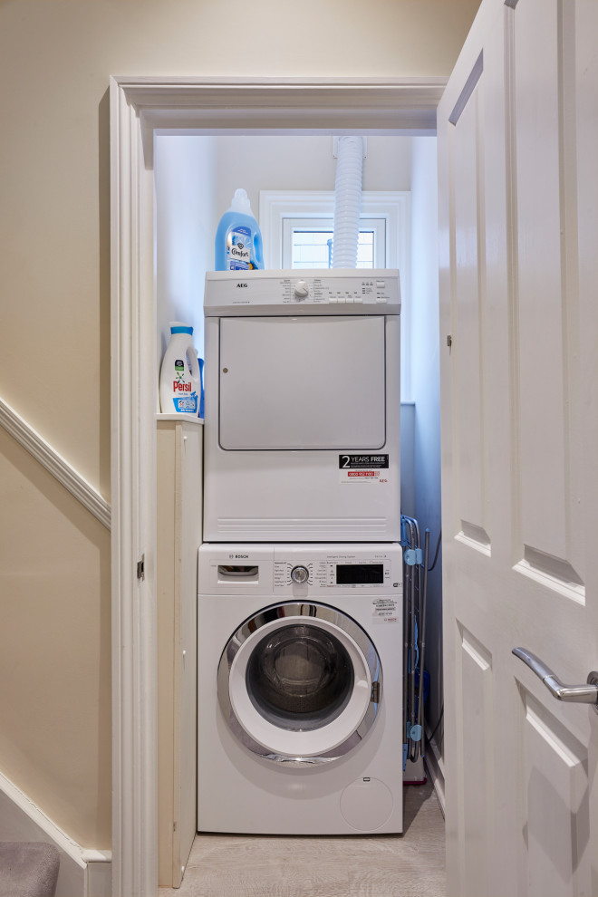 Small contemporary laundry cupboard in London with white walls, laminate floors, a stacked washer and dryer and grey floor.