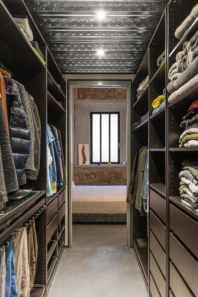 Mid-sized industrial gender-neutral walk-in wardrobe in Barcelona with open cabinets, black cabinets, concrete floors and grey floor.