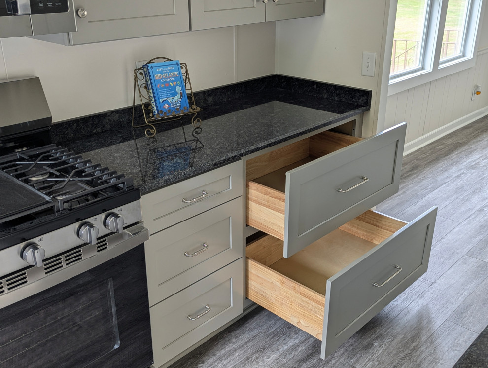 Small transitional l-shaped gray floor enclosed kitchen photo with a single-bowl sink, flat-panel cabinets, gray cabinets, granite countertops, stainless steel appliances and black countertops
