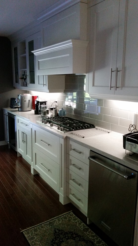 Enclosed kitchen - mid-sized transitional galley dark wood floor and brown floor enclosed kitchen idea in Toronto with recessed-panel cabinets, white cabinets, quartz countertops, beige backsplash, subway tile backsplash, stainless steel appliances and no island