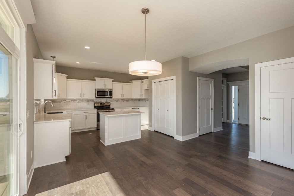 Example of a mid-sized transitional medium tone wood floor and brown floor eat-in kitchen design with an undermount sink, shaker cabinets, white cabinets, quartz countertops, multicolored backsplash, subway tile backsplash, stainless steel appliances, an island and white countertops