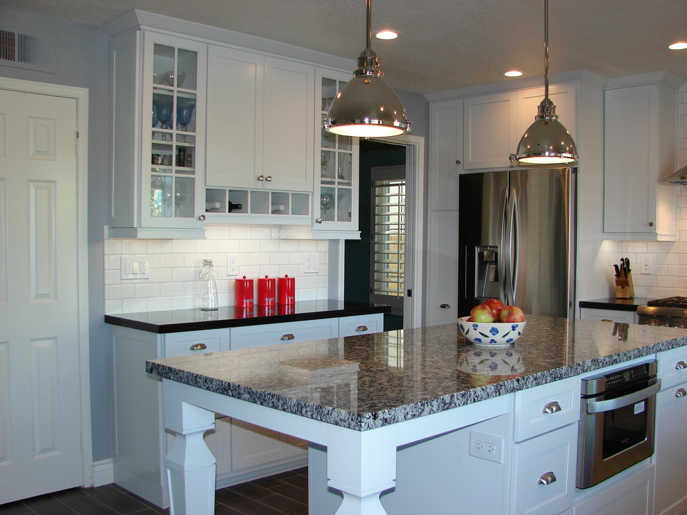Photo of a mid-sized transitional u-shaped eat-in kitchen in Orange County with a farmhouse sink, shaker cabinets, white cabinets, granite benchtops, white splashback, subway tile splashback, stainless steel appliances, porcelain floors and with island.