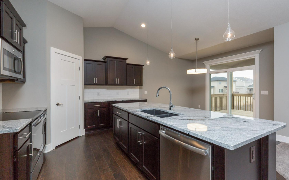 Large transitional dark wood floor and brown floor eat-in kitchen photo with an undermount sink, shaker cabinets, dark wood cabinets, granite countertops, white backsplash, subway tile backsplash, stainless steel appliances, an island and multicolored countertops