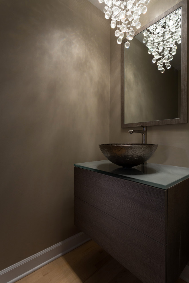 This is an example of a small modern powder room in Chicago with flat-panel cabinets, light wood cabinets, light hardwood floors, a vessel sink, grey walls, glass benchtops and grey benchtops.