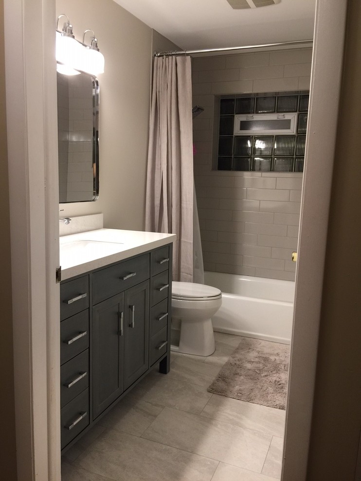 Design ideas for a mid-sized traditional 3/4 bathroom in Chicago with gray tile, porcelain floors, shaker cabinets, grey cabinets, an alcove tub, a shower/bathtub combo, a two-piece toilet, subway tile, grey walls, an undermount sink and solid surface benchtops.
