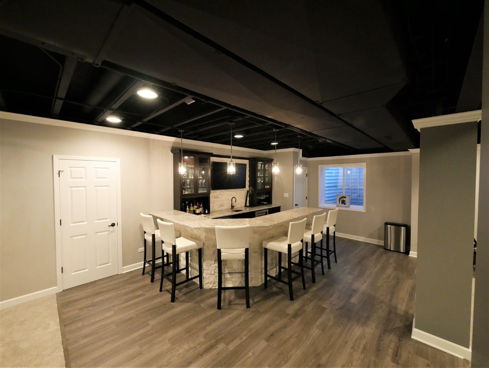 This is an example of a mid-sized transitional l-shaped seated home bar in Chicago with an undermount sink, glass-front cabinets, black cabinets, granite benchtops, white splashback, stone tile splashback, laminate floors, grey floor and beige benchtop.