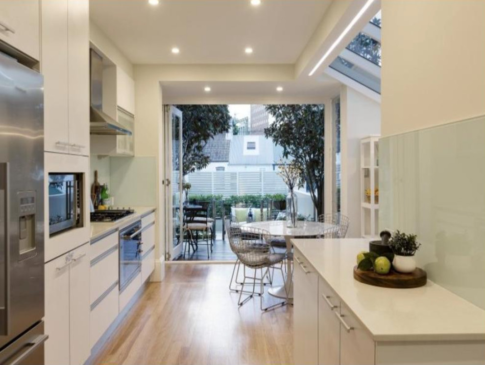 Contemporary eat-in kitchen in Sydney with white cabinets, limestone benchtops, white splashback, ceramic splashback, stainless steel appliances, light hardwood floors and brown floor.